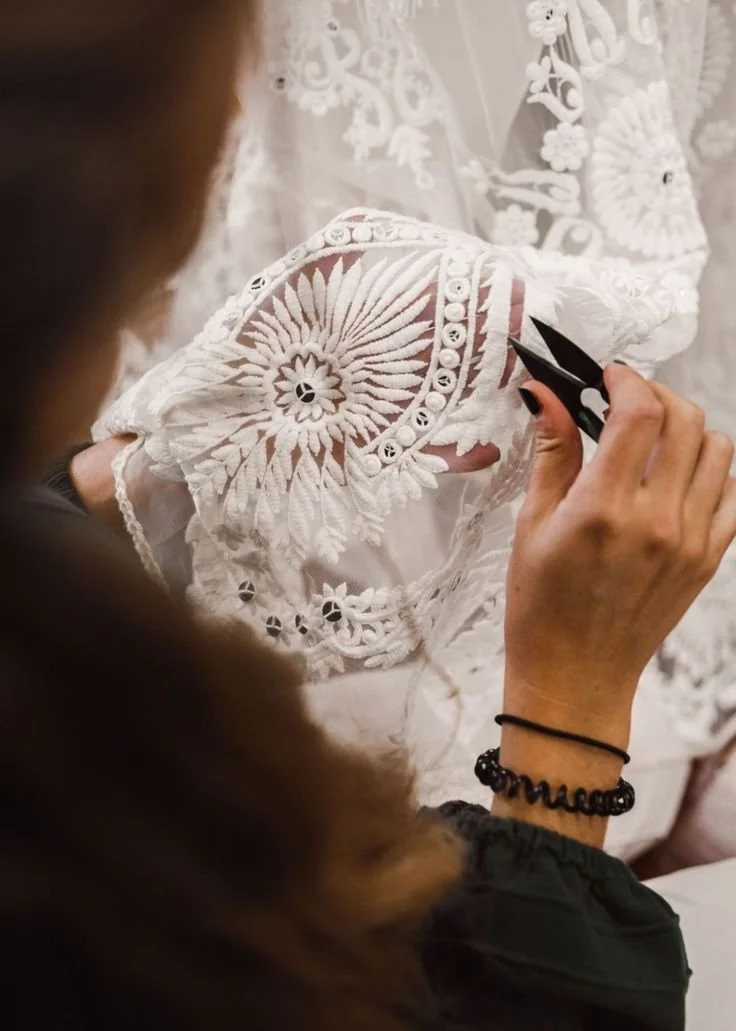Persona trabajando en bordado blanco con diseño floral y detalles de encaje, usando una herramienta de corte.