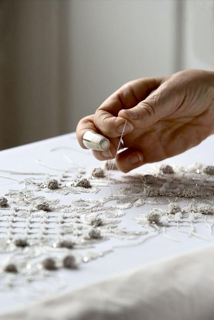 Mano bordando tela blanca con hilo y dedal de costura