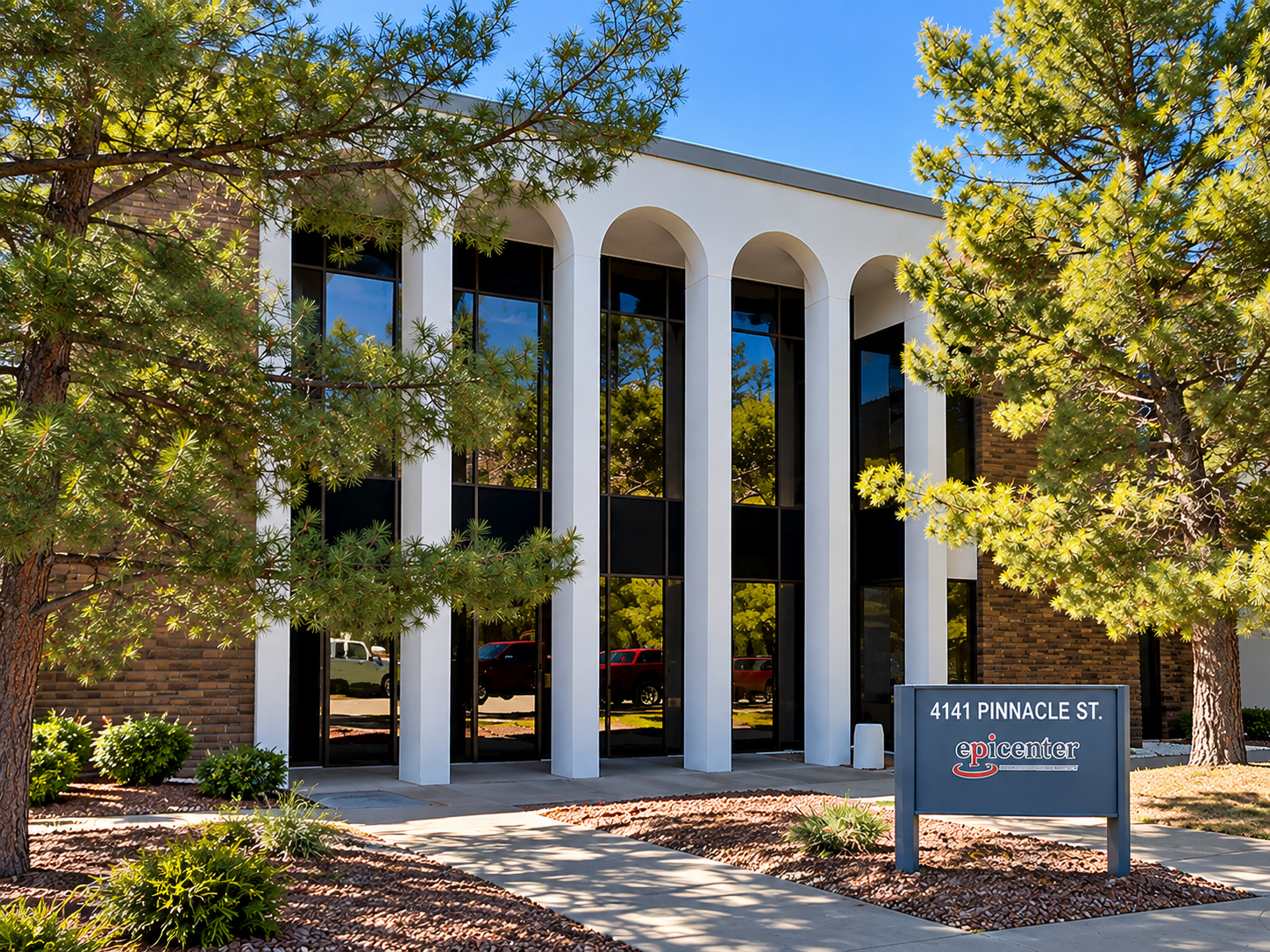 Modern office building with glass windows and white arches, surrounded by trees and shrubs, with a sign that reads '4141 Pinnacle St. Epicenter'.