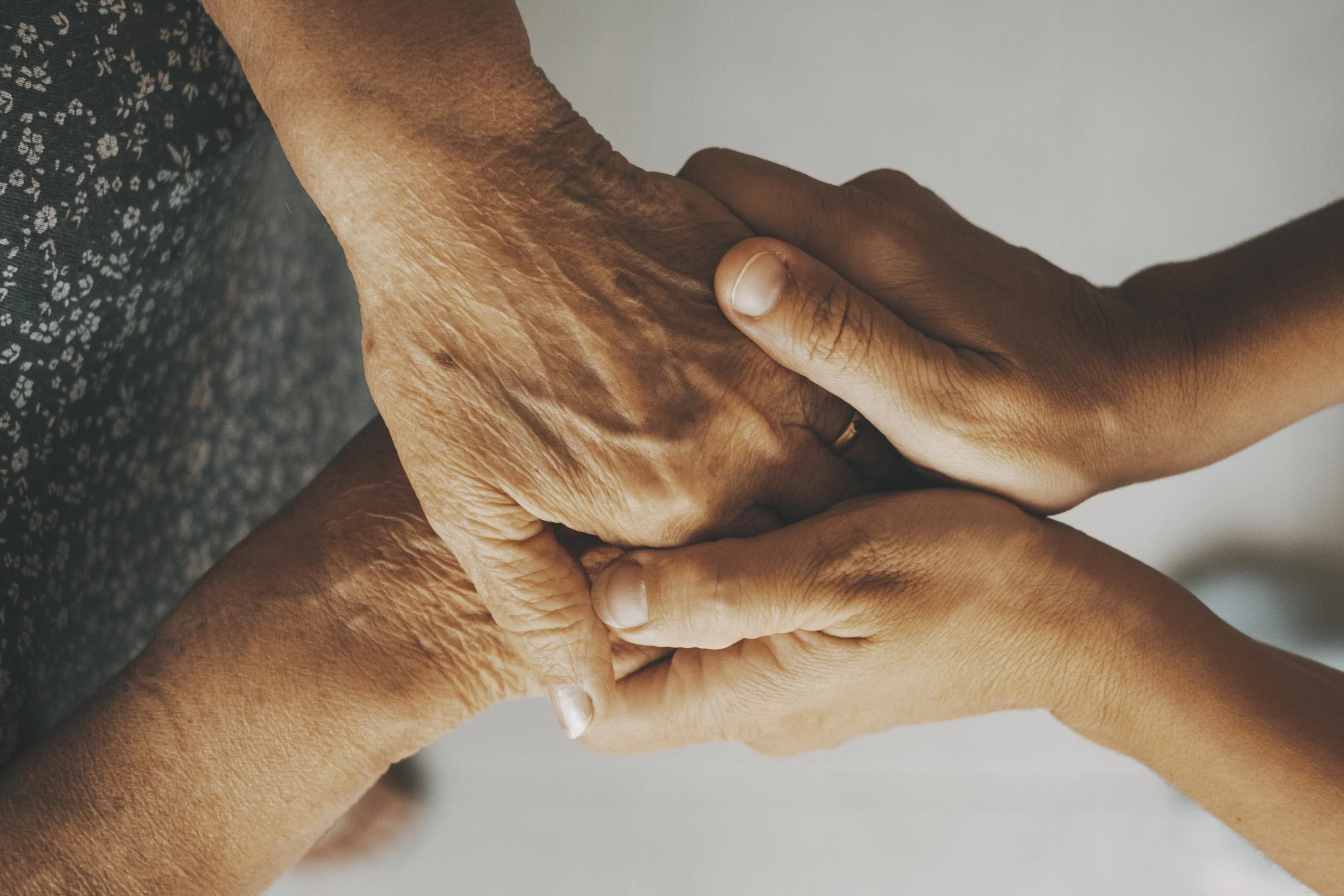 Two people holding hands, one older with wrinkled skin and one younger with smoother skin.