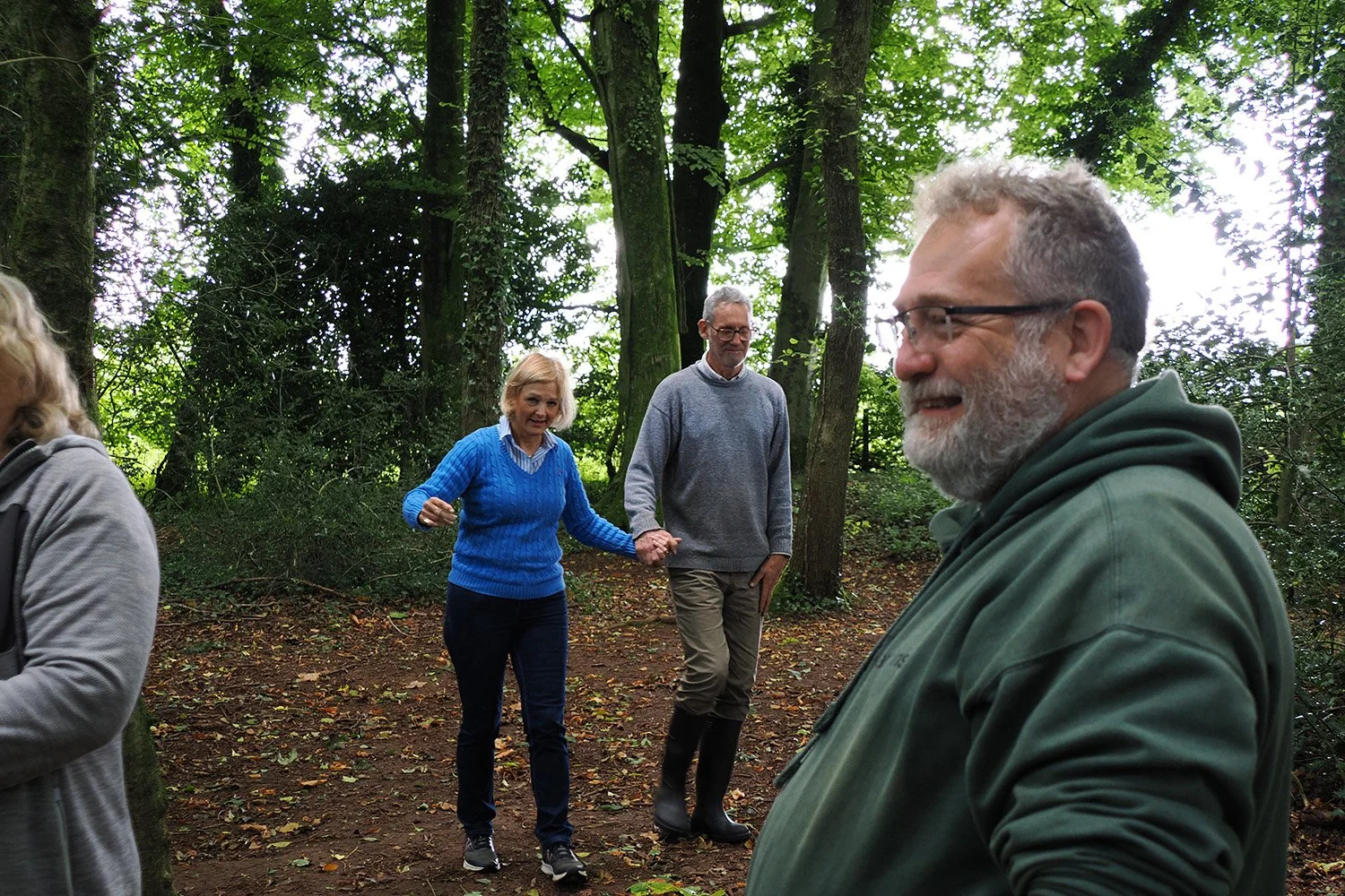 Four people in a forested area, two women and two men, are enjoying an outdoor walk, holding hands and smiling.