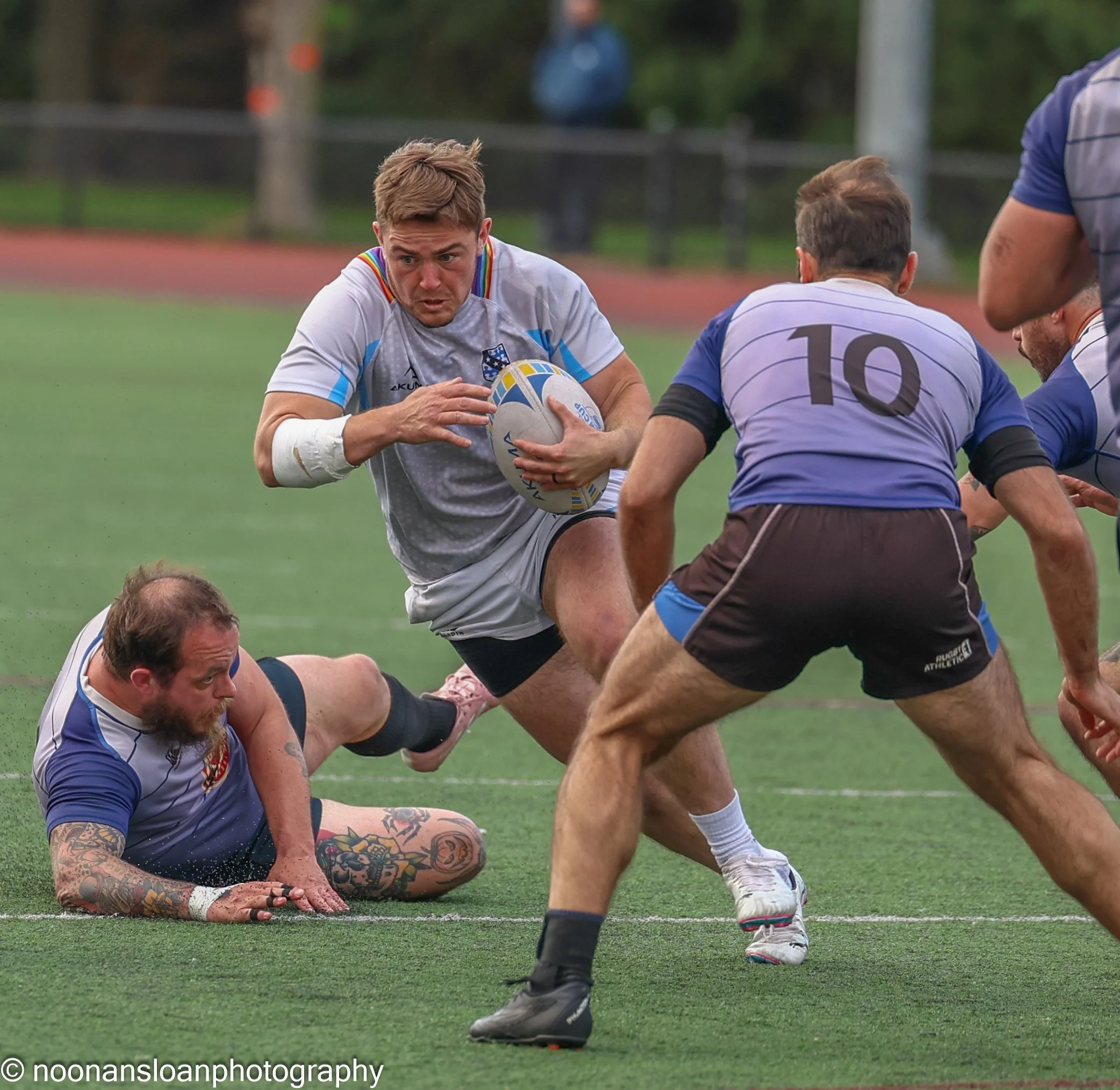 Rugby players competing on the field during a match, with one player holding the ball and others attempting to tackle.