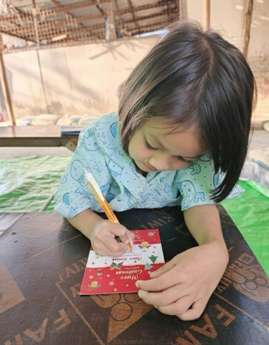 Child writing her Christmas wish card at a CDMN party