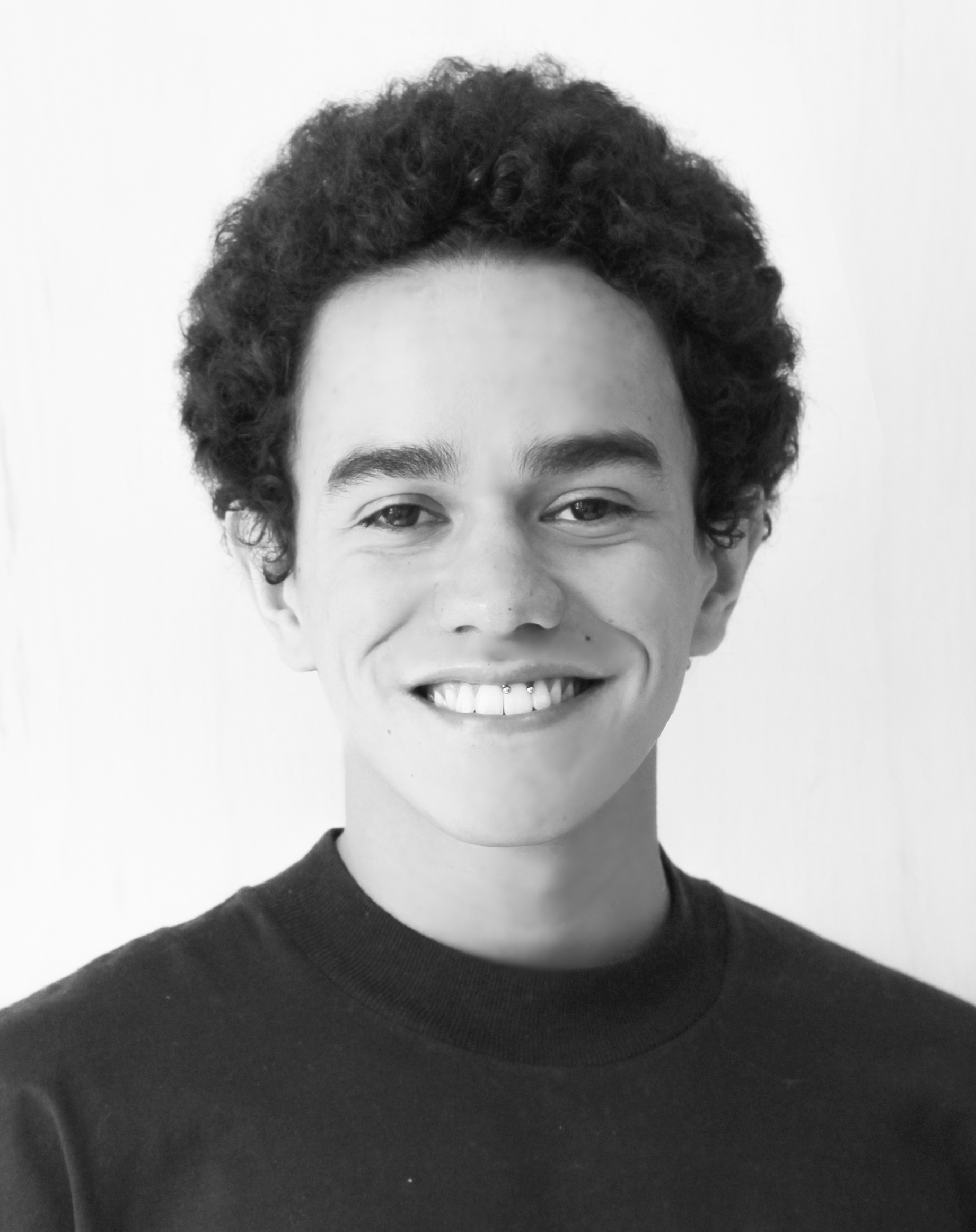 Portrait of a person smiling, wearing a dark shirt, and having curly hair.