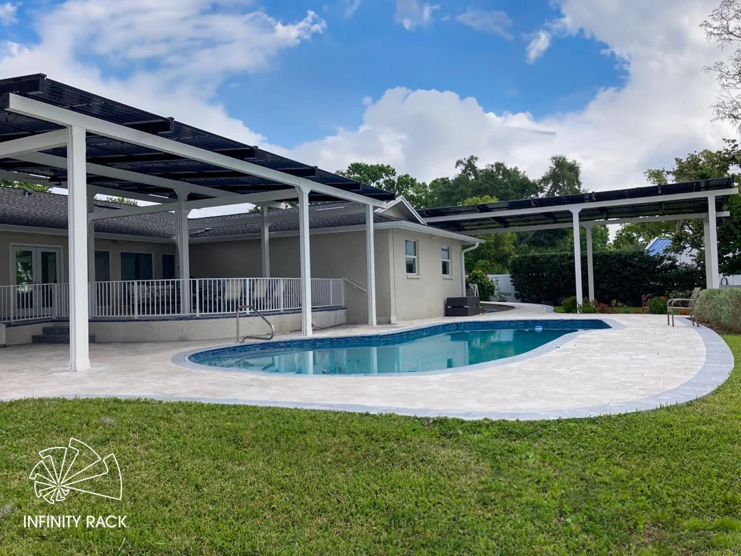 Outdoor patio with furniture under a pergola featuring solar panels, surrounded by lush greenery and palm trees.