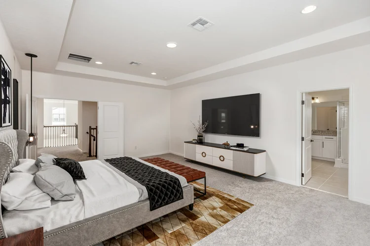 Modern bedroom with a large bed, black throw blanket, and decorative pillows. A bench at the foot of the bed sits on a p