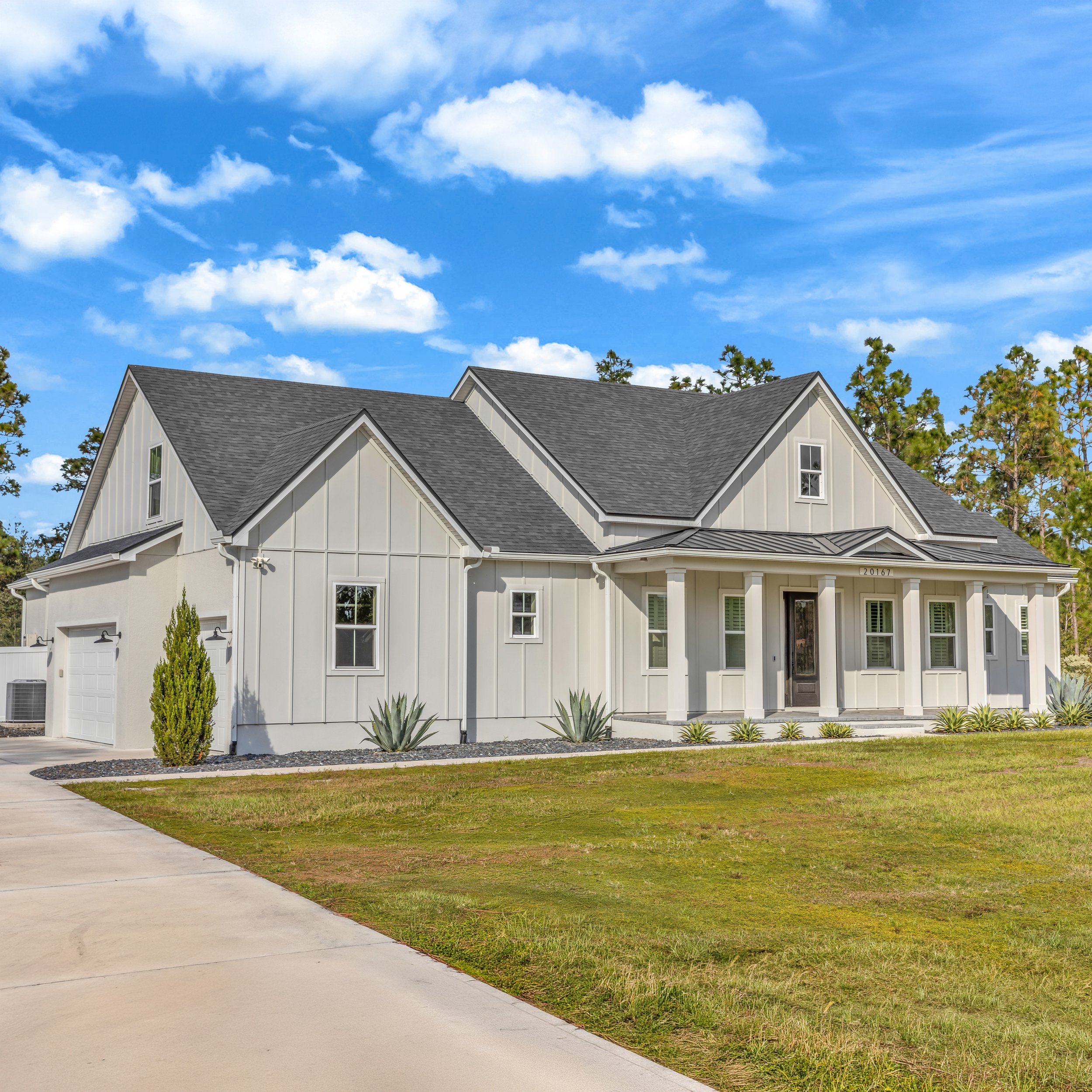 Modern white two-story house with a brown garage door and a landscaped front yard under a clear blue sky.