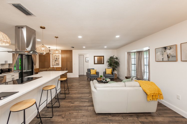Open-concept living room with a white sectional sofa, two gray armchairs with yellow pillows, a round coffee table with 