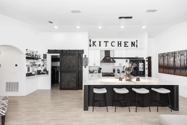 Modern white kitchen with black accents and a large island with four bar stools, stainless steel appliances, decorative 