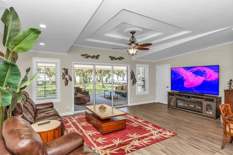 Living room with a large flat-screen TV, leather sofa, wooden coffee table on a red patterned rug, potted plant, and sli