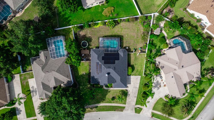 An aerial view of a residential neighborhood showing three houses with backyard pools enclosed in screened structures, s