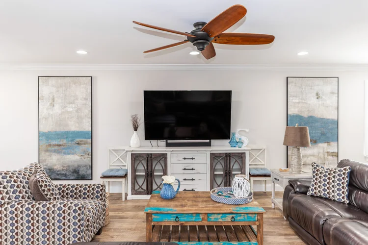 Living room with a wooden coffee table, patterned couches, a wooden TV stand with a large flatscreen TV, decorative vase
