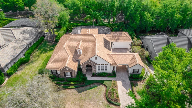 Aerial view of a suburban house with a brown tiled roof, attached garage with solar panels, landscaped front yard, surro