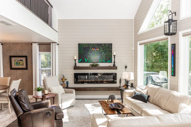 Bright living room with cream sofa, beige armchair, brown leather chair, wooden coffee table, large windows with trees o