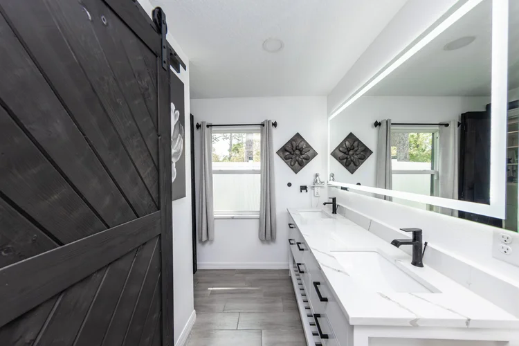 Modern bathroom with white marble countertop, black fixtures, large mirror, gray curtains, and decorative wall art.