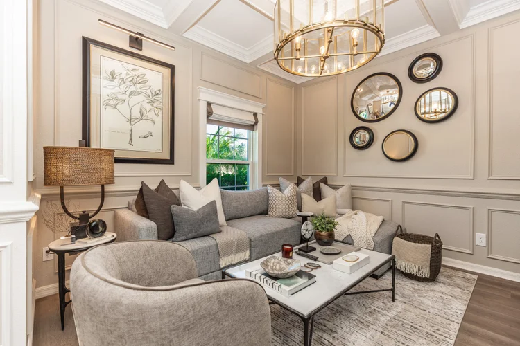 Living room with beige walls, a gray sectional sofa with multiple pillows, a marble coffee table with decor items, a bei