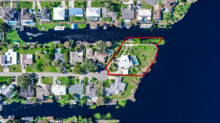 Aerial view of a neighborhood with a house highlighted by a red outline, situated on a waterfront lot with greenery and 