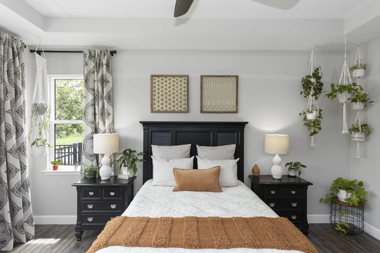 A bedroom with a black bed frame, white bedding, beige and white pillows, and a rust-colored throw blanket. There are ma