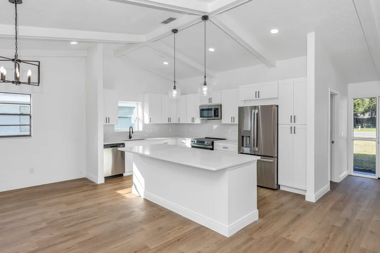 Modern white kitchen with stainless steel appliances, light wood flooring, and a central island with a white countertop.