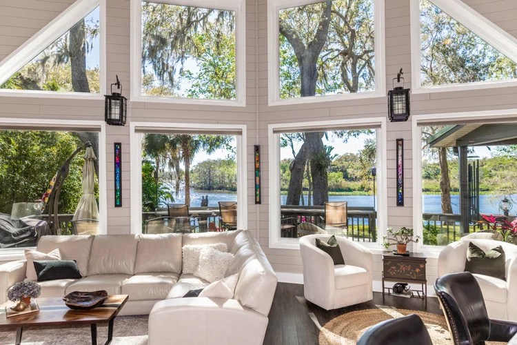 Living room with large windows showing a lakeside view, white leather sofa, white armchair, small side table with potted