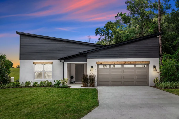 Modern house with dark gray sloped roof, white walls, and a gray garage door, set against a colorful sunset sky and gree