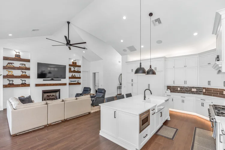 Open-concept living room and kitchen with white cabinetry, a kitchen island, black pendant lights, dark wood flooring, a