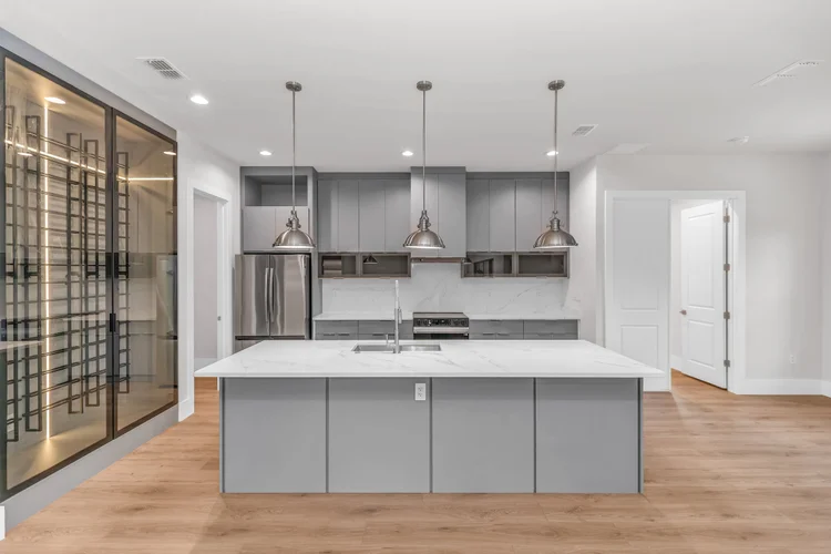 Modern kitchen with gray cabinets, white marble island, stainless steel appliances, pendant lighting, and hardwood floor