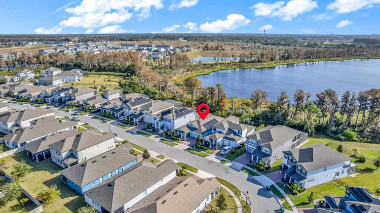 Aerial view of a suburban neighborhood near a lake, with modern houses and solar panels on rooftops, surrounded by trees