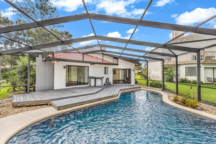 Backyard with a swimming pool enclosed by a screened structure, adjacent to a white house with sliding glass doors and a