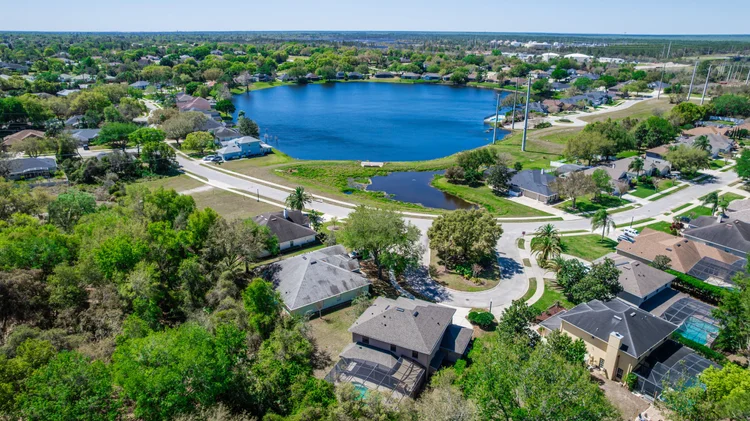 Aerial view of a suburban neighborhood surrounding a large man-made lake, with houses, trees, and streets visible.