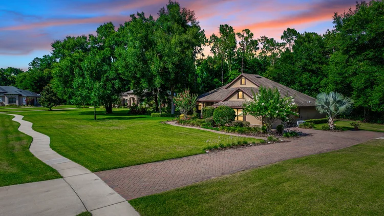 Suburban house surrounded by well-maintained lawn and trees during sunset.