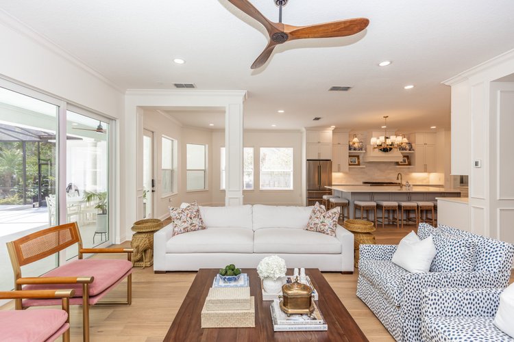 Living room with white sofa, patterned armchair, wooden coffee table, and view into the kitchen with island and bar stoo