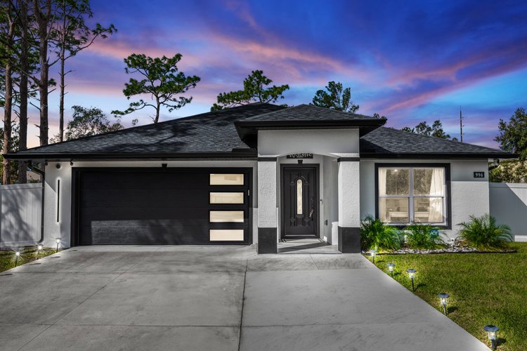 Modern single-story house with white and black exterior, black garage door with rectangular windows, concrete driveway, 