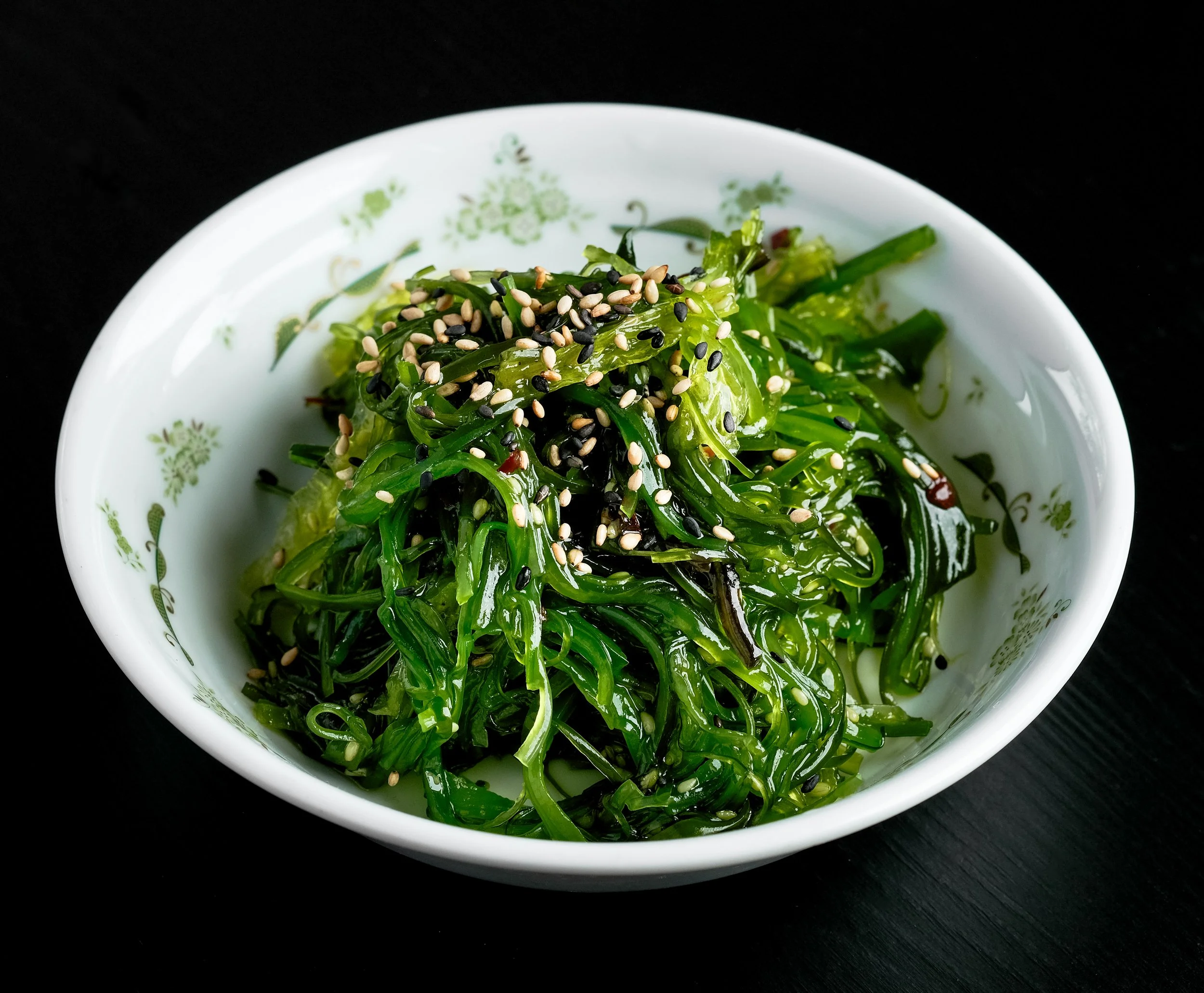 Seaweed salad topped with sesame seeds in a white floral bowl