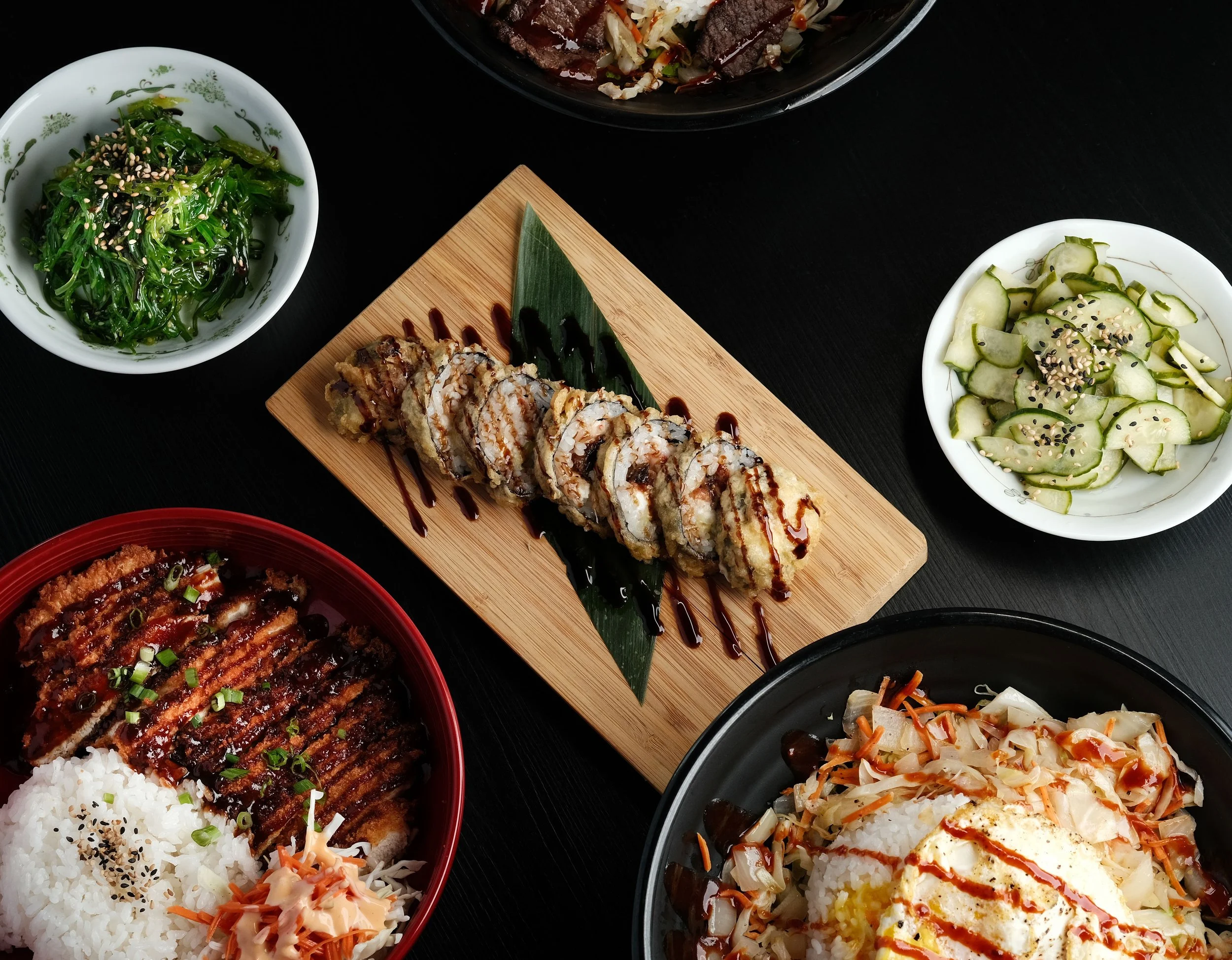 assorted Japanese dishes including sushi rolls, rice bowls, seaweed salad, cucumber salad, and a vegetable stir-fry