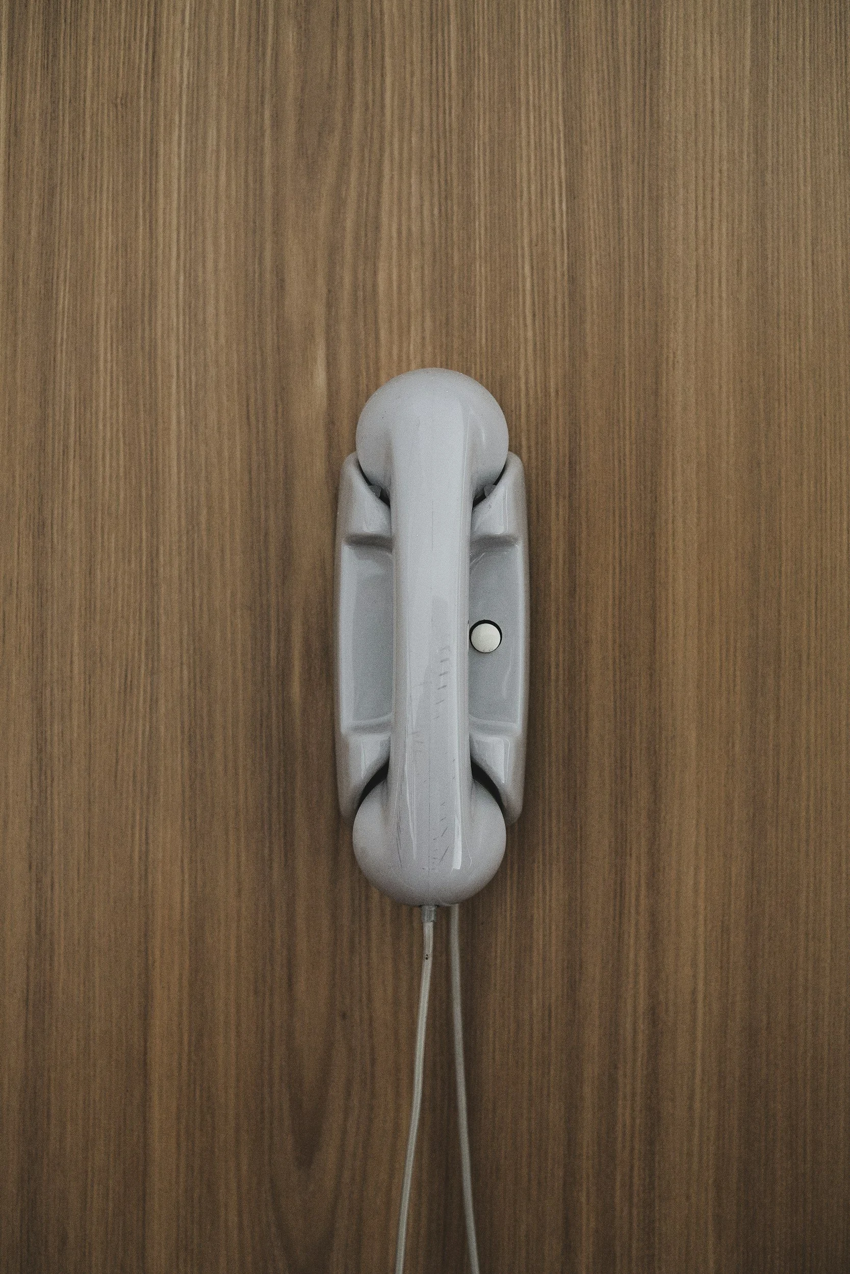 A white landline telephone mounted on a wooden wall.
