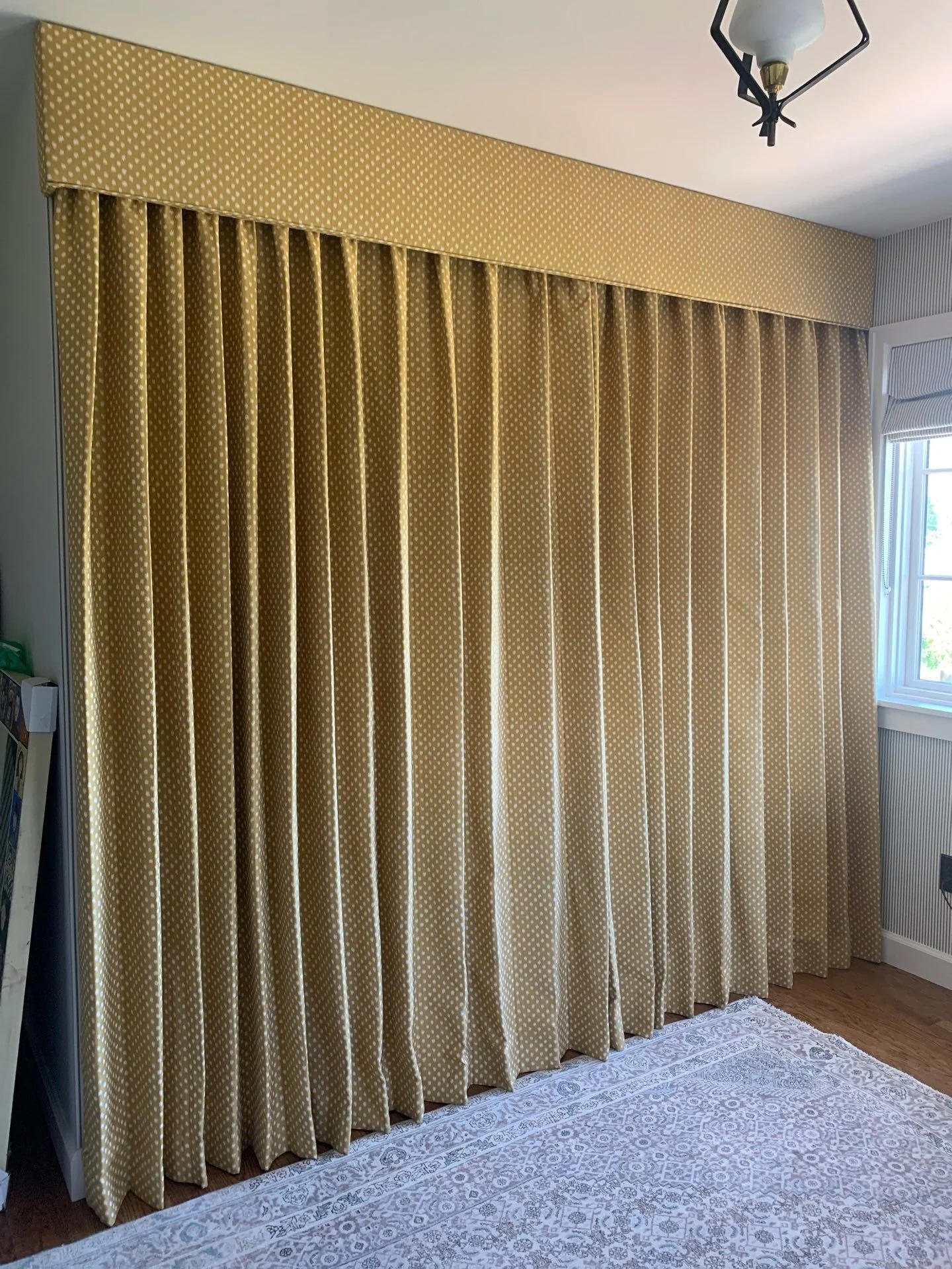 Pleated drapery panel topped with a valance with welt trim across.