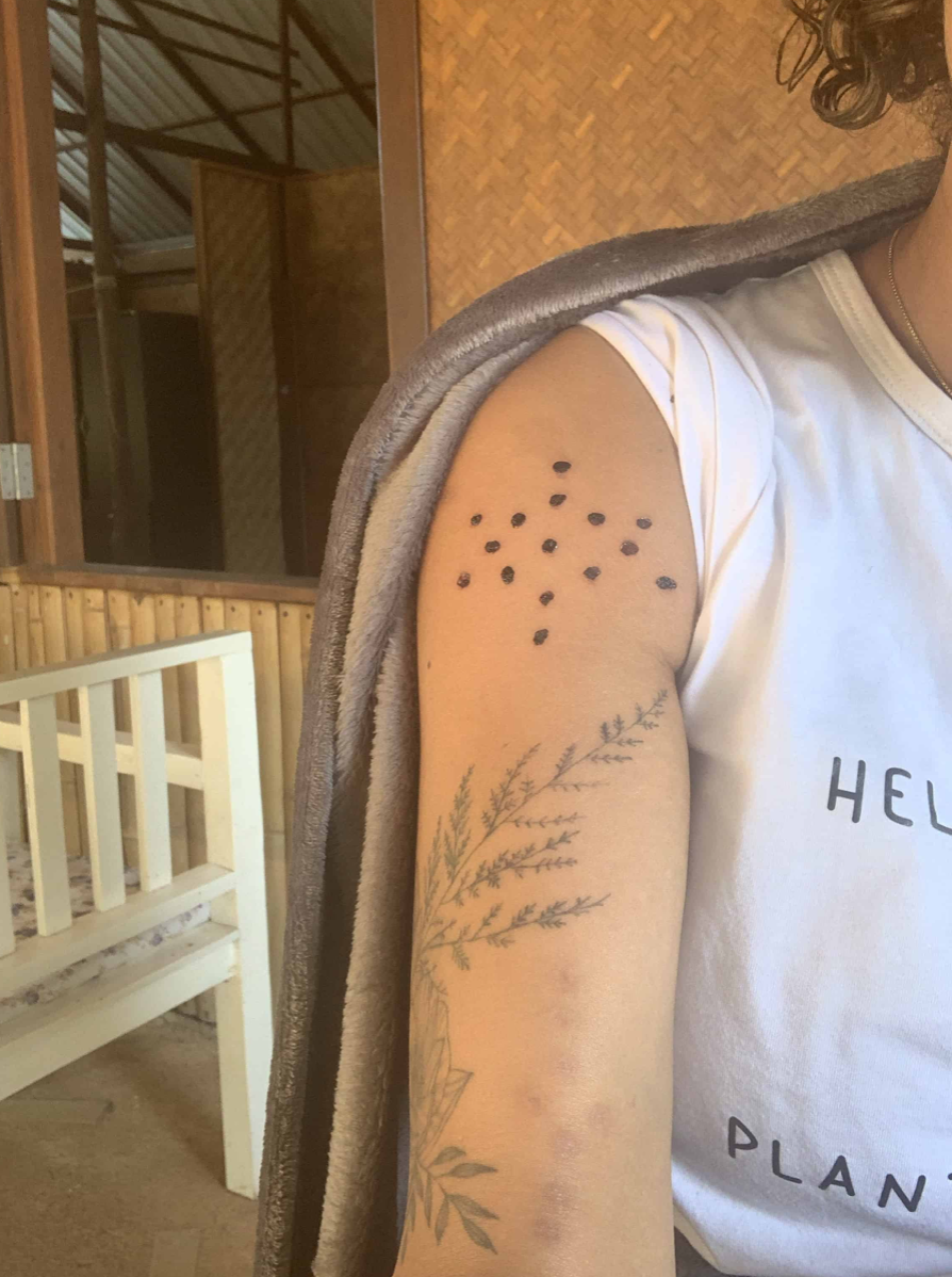 Person's arm with kambo and floral design, wearing a white shirt, indoors with wooden background.
