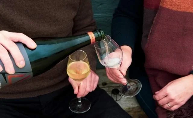 Two people pouring a glass of Bubbles of Britain wine.