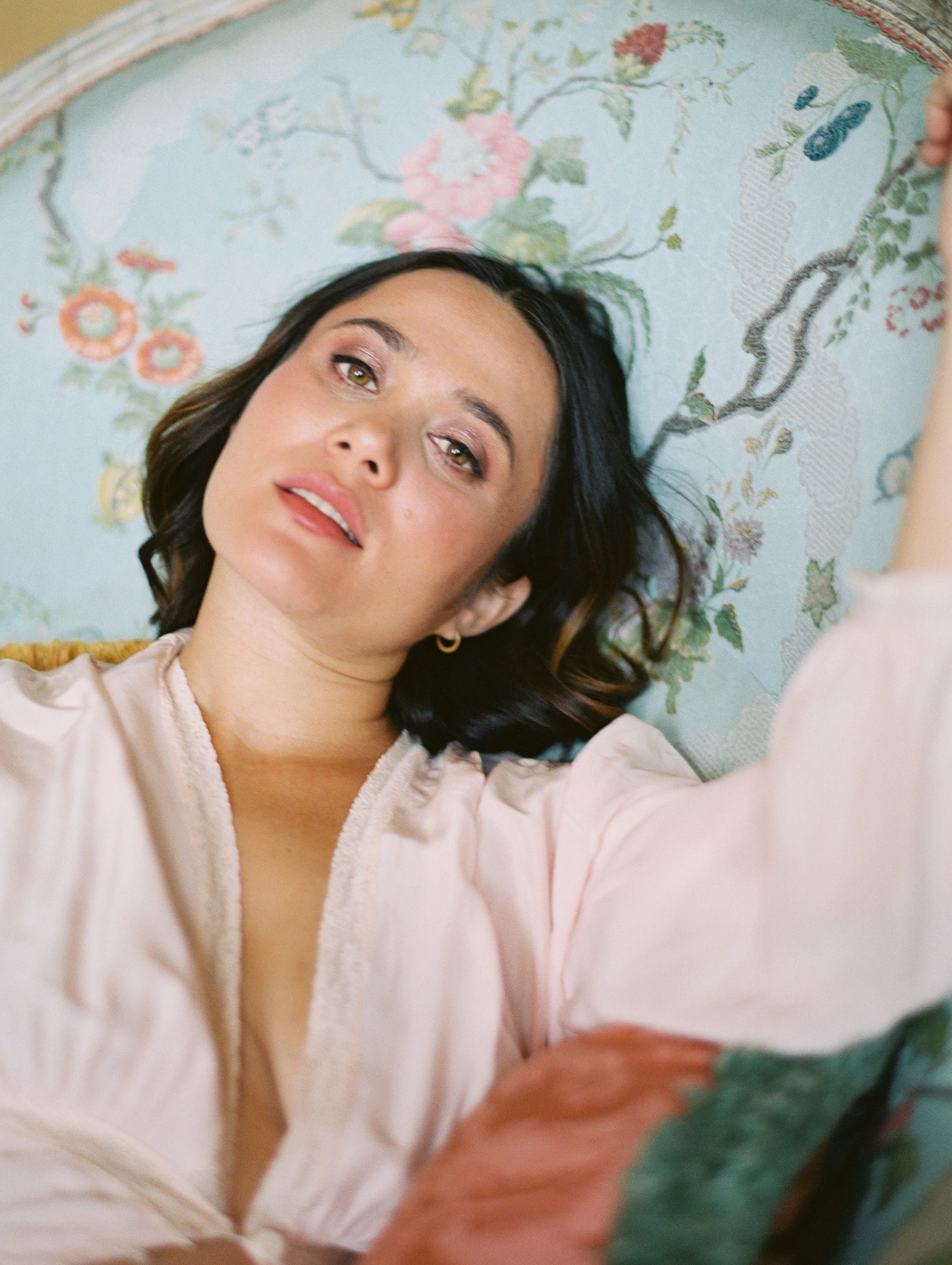 A pregnant woman poses on a​n antique​ French chaise. She wears a pale pink robe ​and she gazes directly at the camera.
