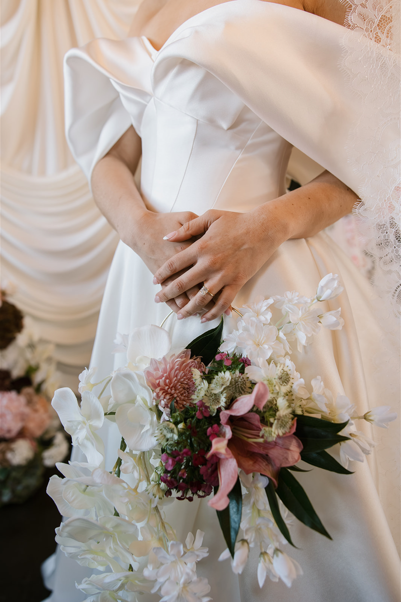 TheBloomeryKC.com. Close-up of a bride in a white wedding gown holding a bouquet of white, pink, and green flowers.