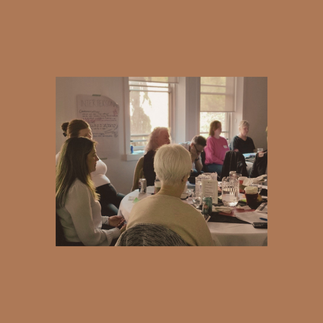People sitting around tables in a meeting room with dim lighting meditating with their eyes closed.