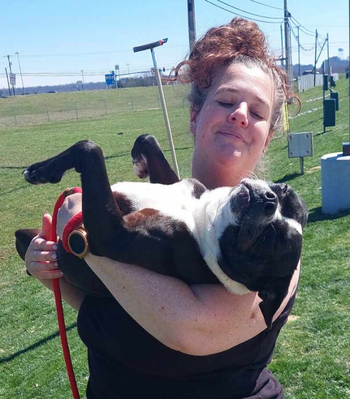 Lady holding medium sized black and white dog in field