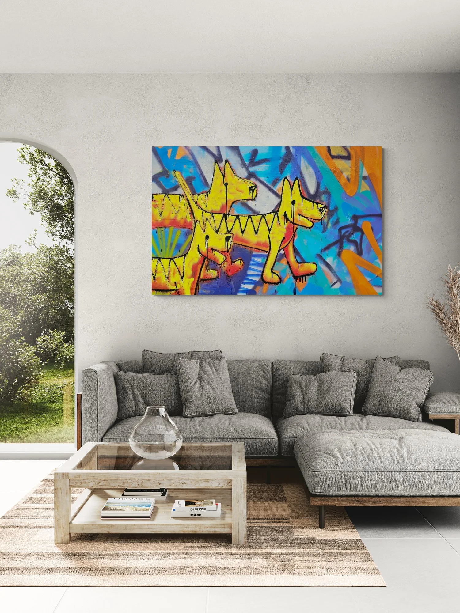 Modern living room with gray couch, glass vase, coffee table with books, and colorful graffiti-style art of three yellow dogs on the wall.