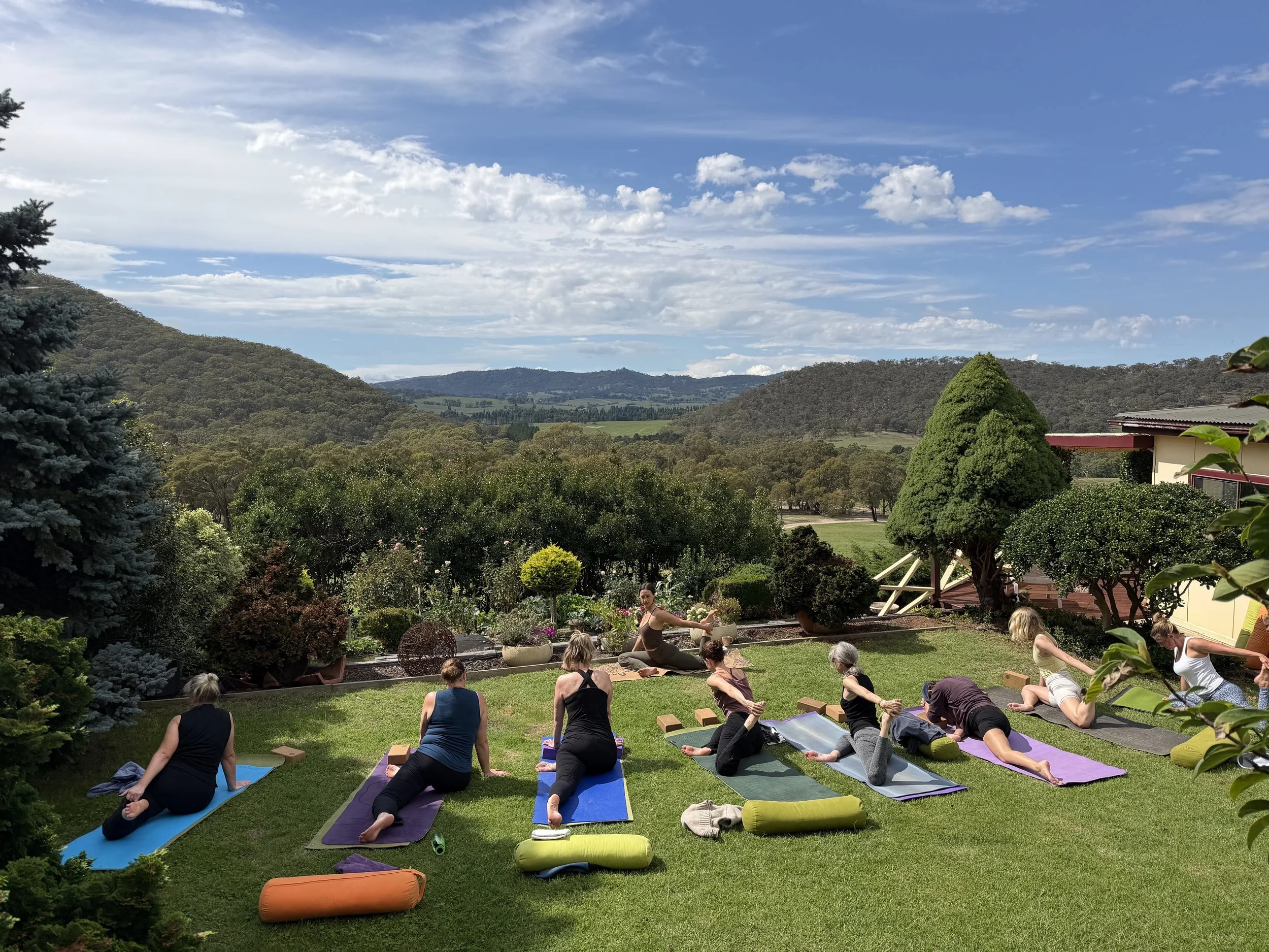 a group of people doing yoga on a lawn overlooking a sprawling valley