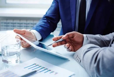 Two business professionals reviewing documents and a tablet at a desk with a glass of water.