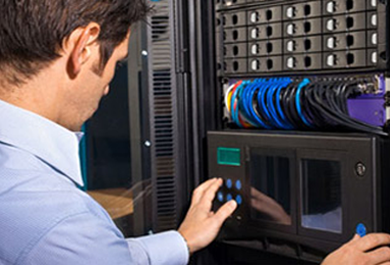 A man operating a touchscreen control panel in a server room with server racks and cables.