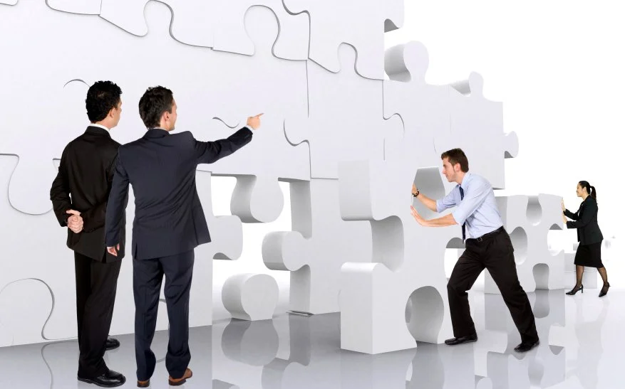Four businesspeople working together to assemble a large jigsaw puzzle wall.