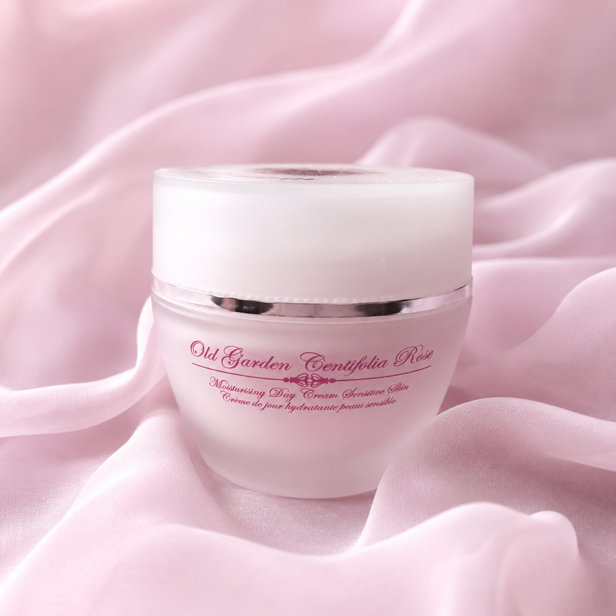 A pink jar of Old Garden Centifolia Rose moisturizing day cream resting on pink silky fabric.
