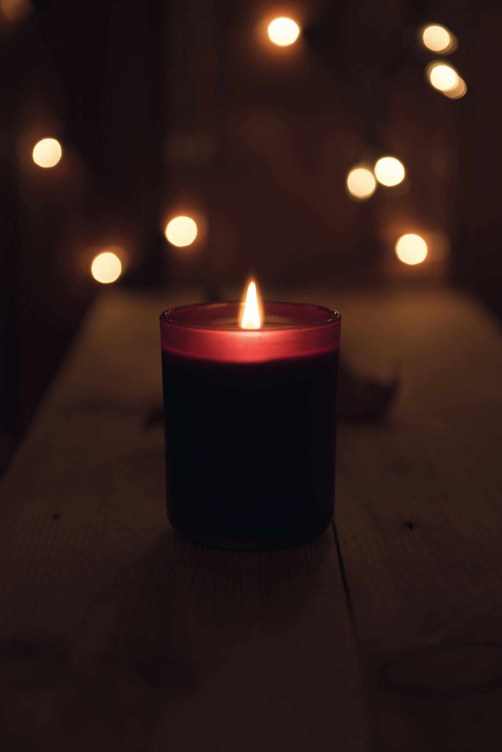 Une bougie allumée sur une table dans une pièce sombre, avec des lumières floues en arrière-plan.